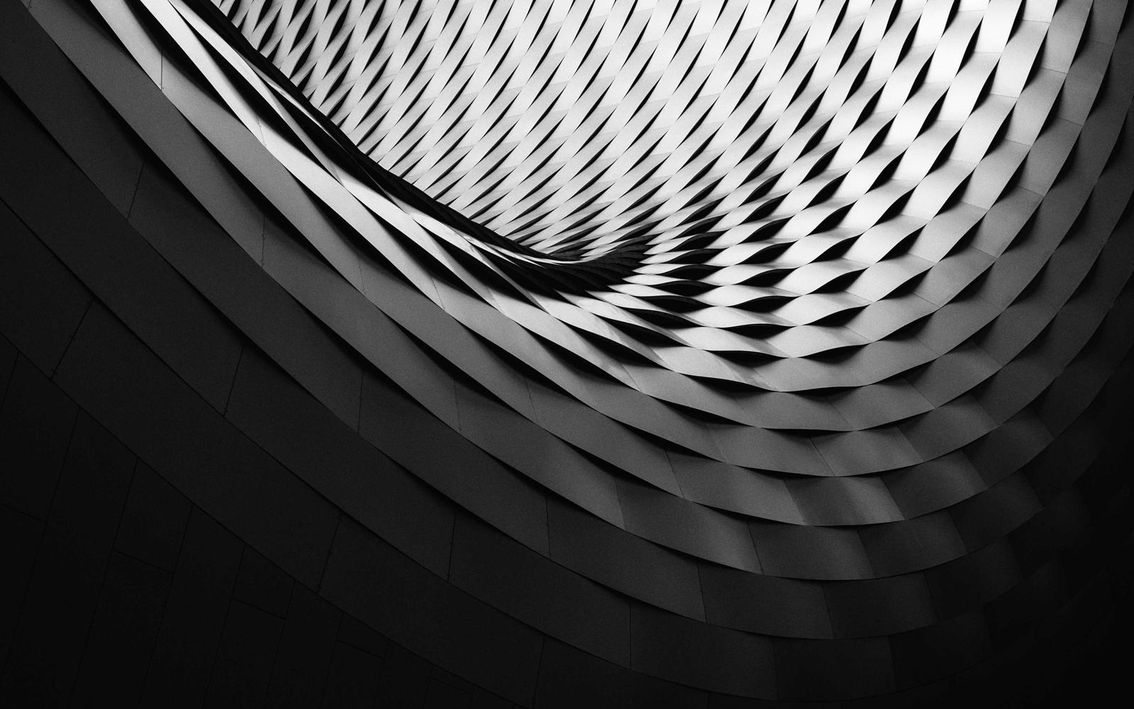 A finished building facade of woven metal bands curving overhead